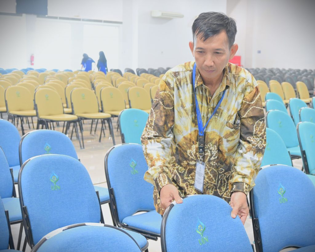 Pegawai senior multitalenta Hadi Rustami saat merapikan kursi para peserta wisuda (Foto:Humas/Jamal Ripani)